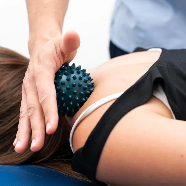 Fysioterapeut bruker massasjeball på pasientens skulder.